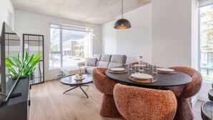 A modern living room with a round dining table, grey sofa, and a large window. - The Velvet Loft Montréal (Montreal)