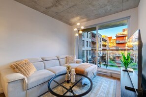 A modern living room with a sofa, a glass coffee table, and a view of a cityscape through large windows.