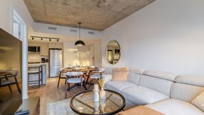A modern living room with a sofa, a glass coffee table, a dining area with a round table and chairs, and a kitchen in the background. - CityGlow Montréal w/ Free Parking (Montreal)