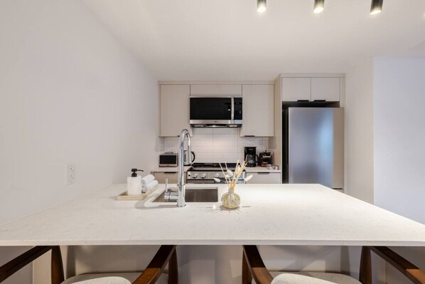 A modern kitchen with white cabinetry, stainless steel appliances, and a central island.