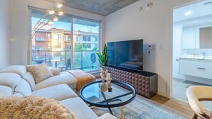 A modern living room with a sofa, a glass coffee table, a TV, and a balcony with a view of buildings. - CityGlow Montréal w/ Free Parking (Montreal)