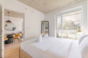 A modern hotel room with a large bed, a dining area with a round table and chairs, a large window with a view, and a balcony. - The Downtown Escape Montréal (Montreal)