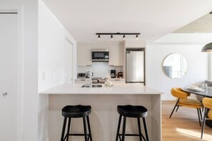 Une cuisine moderne avec des meubles blancs, un îlot central doté de tabourets et un coin repas avec une table ronde et des chaises jaunes.