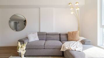 Een moderne zithoek met een grijze modulaire bank, een ronde spiegel, een vloerlamp en een vaas met gedroogde bloemen.