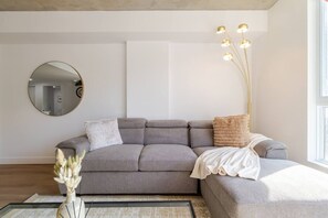 A modern living room with a grey sectional sofa, a round mirror, a floor lamp, and a vase with dried flowers. - The Downtown Escape Montréal (Montreal)
