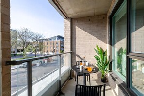 Ein Balkon mit Tisch, Stühlen, einem Blumentopf und Blick auf die Straße und die Gebäude.