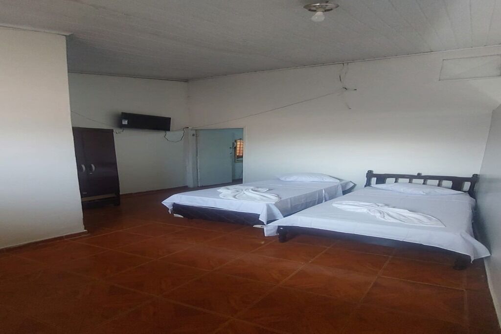 A room with two beds, a ceiling fan, a television mounted on the wall, and a door leading to another room.