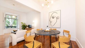 A dining area with a round table, six chairs, a television, and a large abstract painting. - Cheese&Wine™ | Amoreiras Garden 3 (Lisbon)