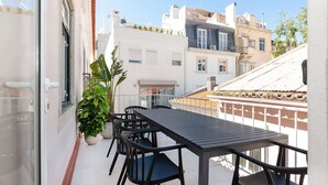 A balcony with a table and chairs, potted plants, and a view of neighboring buildings. - Cheese&Wine™ | Amoreiras Garden 3 (Lisbon)