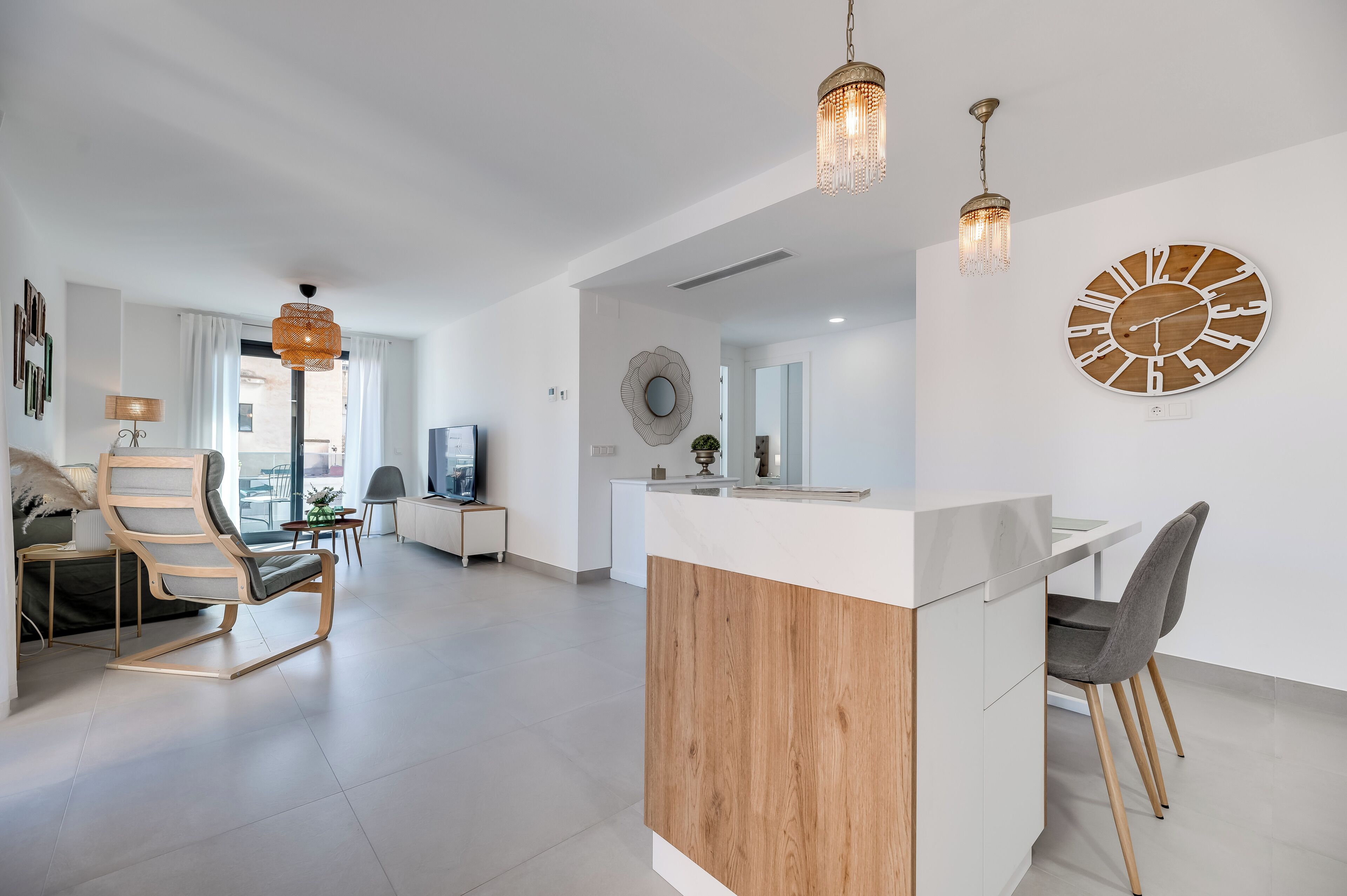 Uma sala de estar moderna com área de jantar de madeira, um relógio grande e uma luminária pendente.