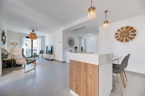 A modern living room with a wooden dining area, a large clock, and a hanging light fixture. - LXR Indico 2-Bedroom Apartment by the Sea (Fuengirola)