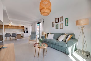 Ett modernt vardagsrum med en soffa, ett soffbord och en matplats med stolar, och ett kök syns i bakgrunden.