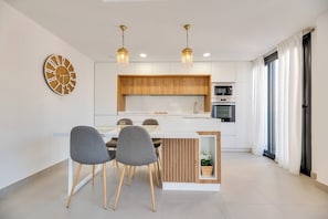 A modern kitchen with a central island, pendant lighting, and a dining area with chairs. - LXR Indico 2-Bedroom Apartment by the Sea (Fuengirola)