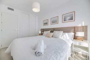 A neatly made bed with white linens and a rolled towel, a bedside table with a lamp, and a wall-mounted picture frame. - LXR Indico 2-Bedroom Apartment by the Sea (Fuengirola)
