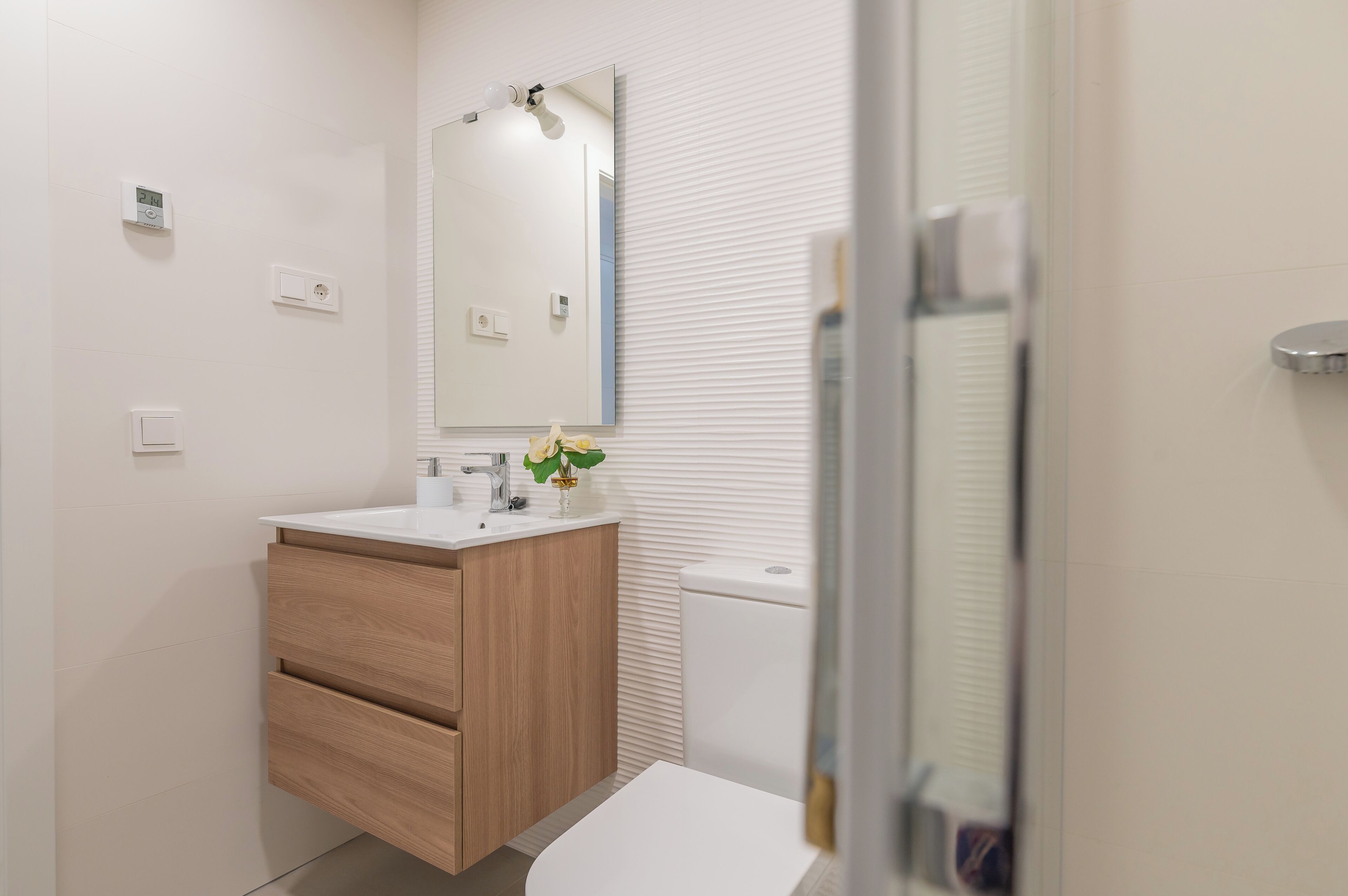 Un baño con lavabo blanco, mueble de madera y espejo.