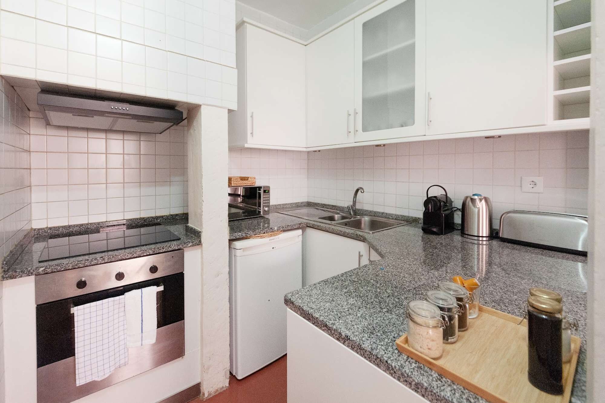 Een keuken met witte kastjes, een roestvrijstalen oven, een magnetron, een broodrooster en een koffiezetapparaat.