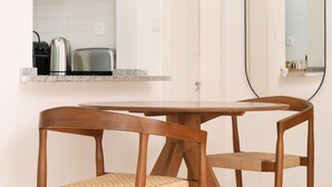 Eine moderne Küche mit weißen Schränken, einem Edelstahl-Wasserkocher und einem Toaster. Ein runder Holztisch mit zwei Stühlen und einer Pendelleuchte.