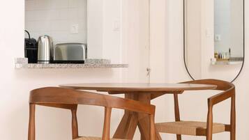 Een moderne keuken met witte kasten, een RVS waterkoker en een broodrooster. Er staat een ronde tafel met twee houten stoelen en een hanglamp.
