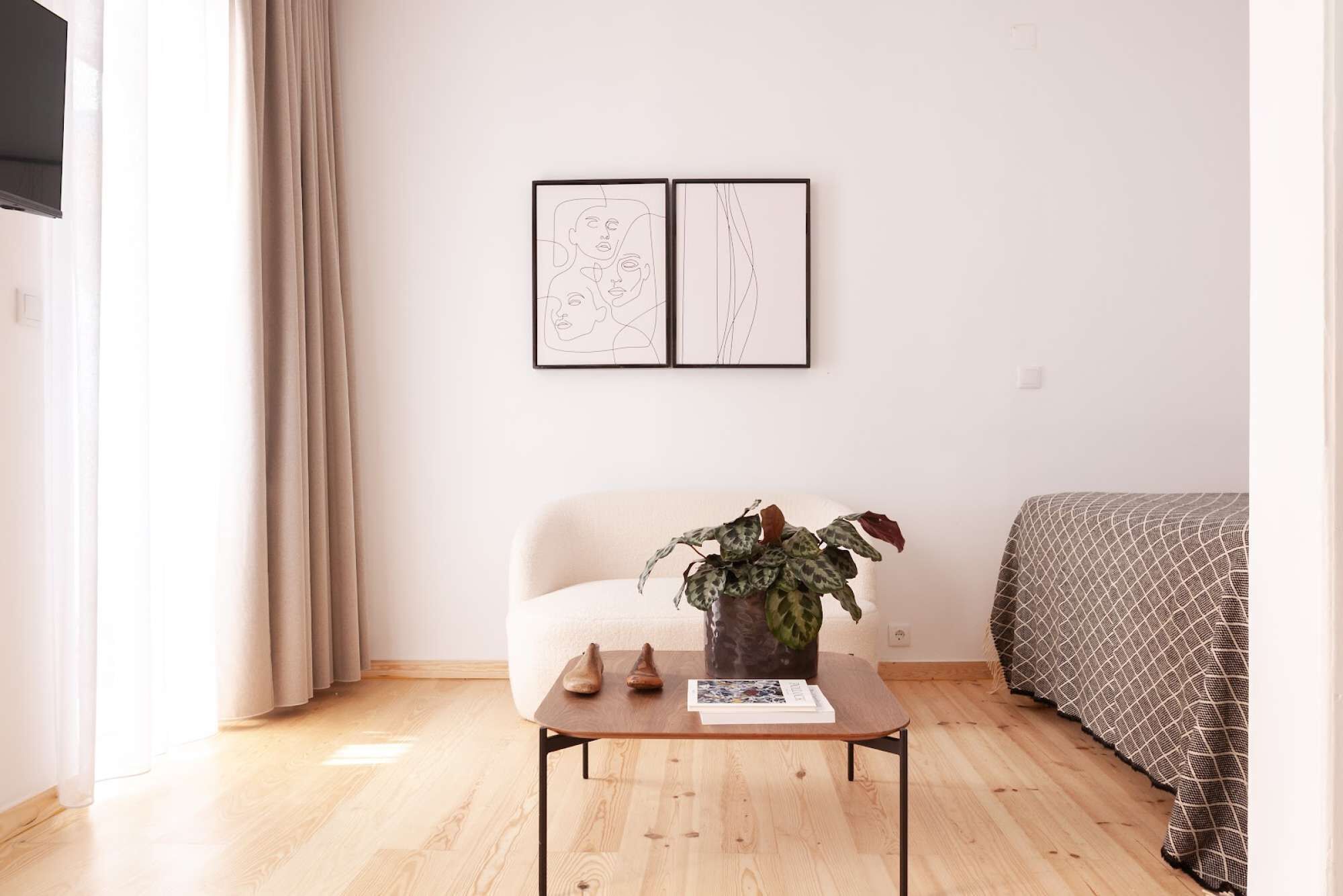Een kamer met een bed, een stoel, een tafel met een plant en twee kunstwerken in lijsten aan de muur.
