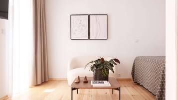 Een kamer met een bed, een stoel, een tafel met een plant en twee kunstwerken in lijsten aan de muur.
