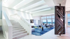 A spacious living area with a staircase, a large window overlooking the ocean, and a modern design.