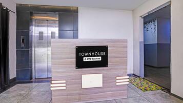 Ein Empfangsschalter mit einem Schild, auf dem 'TOWNHOUSE OYO-Serviced' steht, in einem modernen Gebäude mit Aufzügen und einem gemusterten Boden.