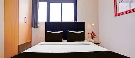 Una habitación de hotel con una cama, una mesita de noche, un ventanal con cortinas, una lámpara de pared y un cuadro enmarcado.