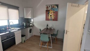 Een praktische keuken met een wasmachine, een eethoek met twee stoelen, en een deur naar een andere kamer.