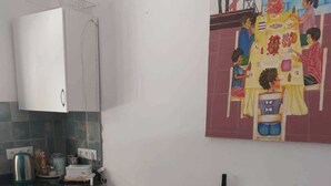 Uma cozinha compacta com máquina de lavar, uma mesa de jantar de madeira e um mural na parede.
