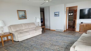 Ett vardagsrum med en beige soffa, en mönstrad matta, ett soffbord i trä och en tv.