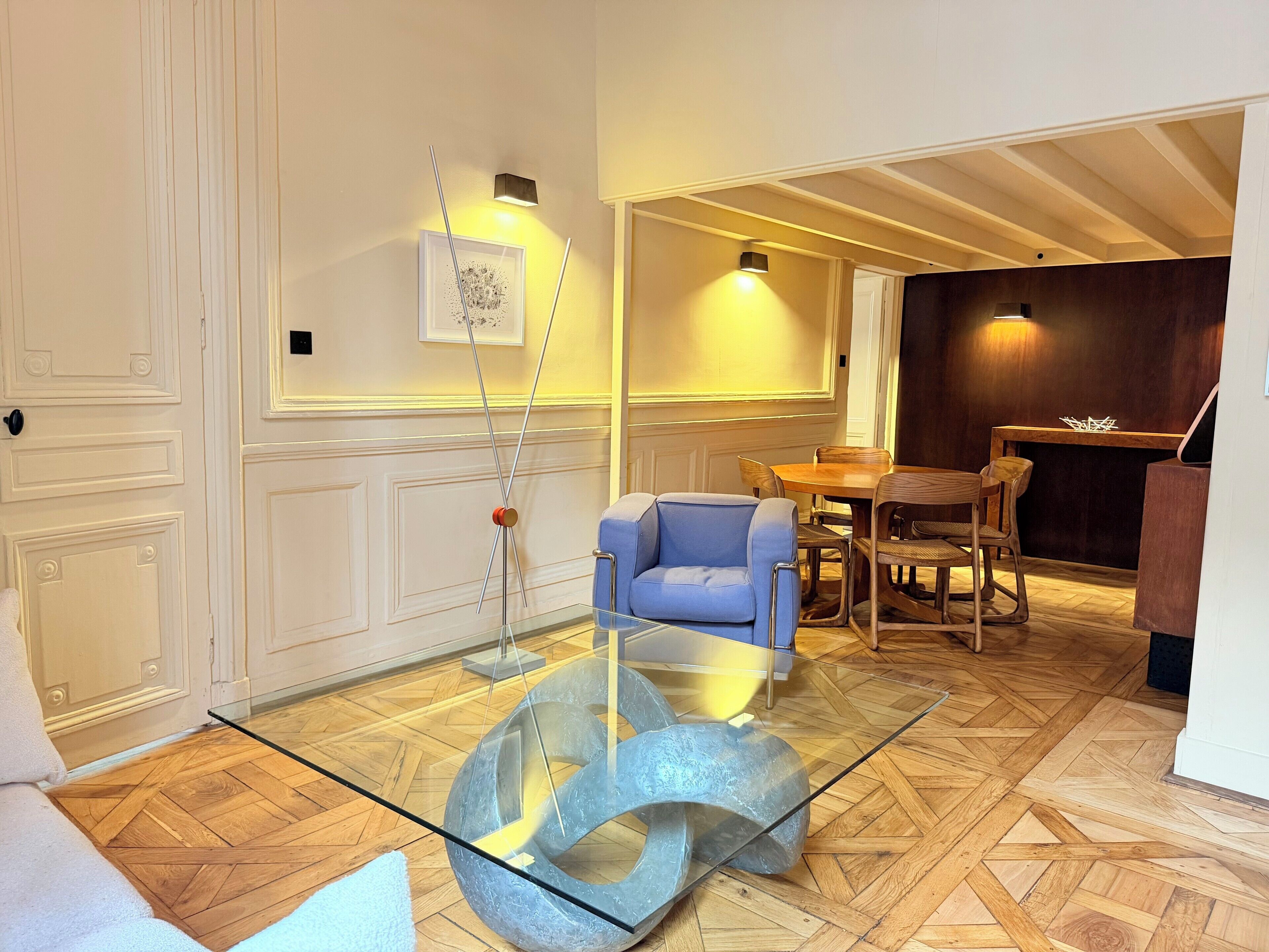Een modern interieur met een glazen salontafel, een blauwe bank en een houten eettafel.