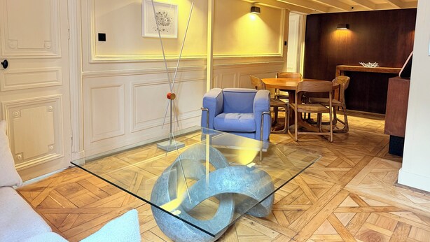 Een modern interieur met een glazen salontafel, een blauwe bank en een houten eettafel.