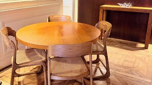 Een ronde houten tafel met vier stoelen, een klein rechthoekig tafeltje en een deur met lichtschakelaar.