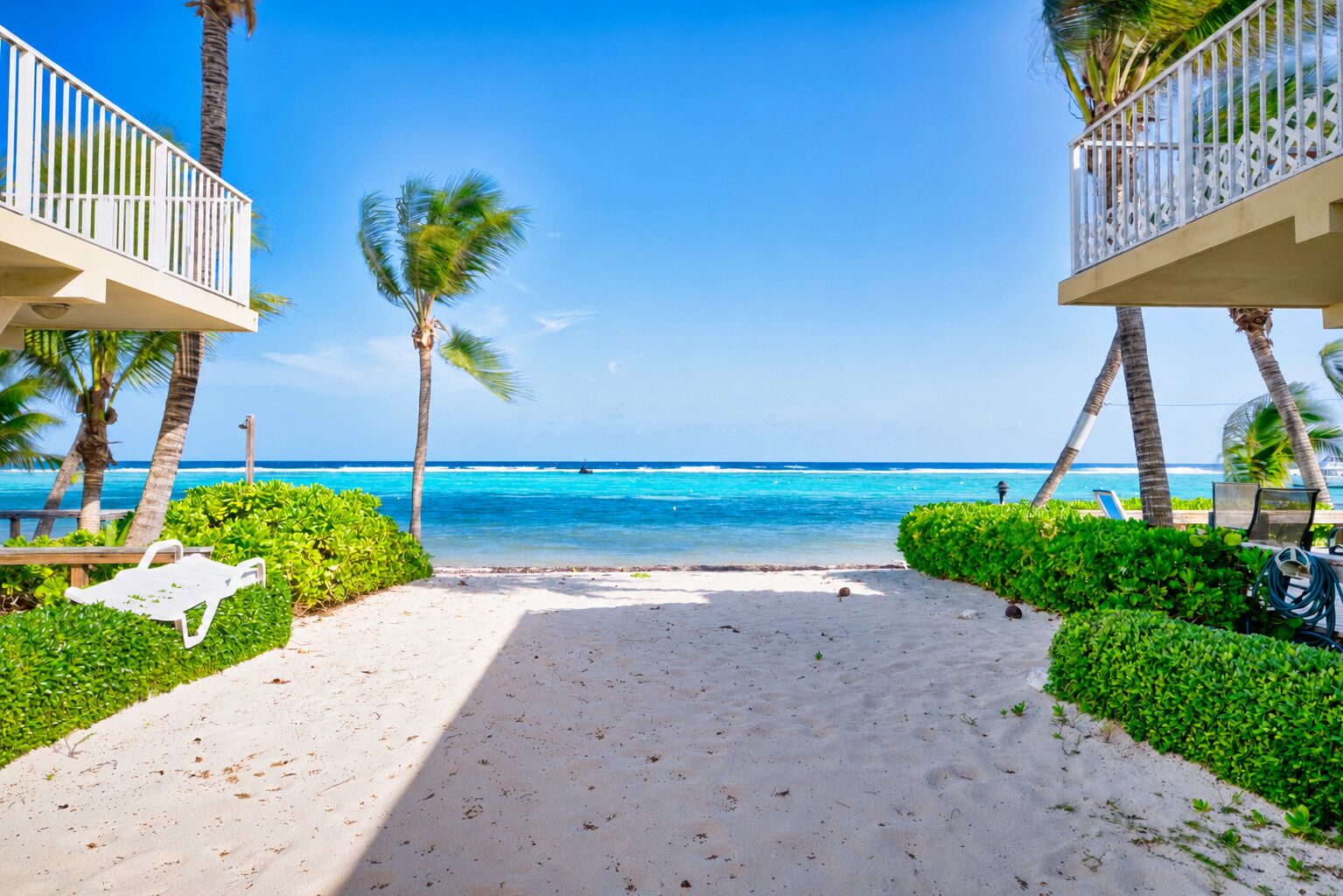 Vista sulla spiaggia con un sentiero che conduce verso l'oceano, palme e una sedia bianca.