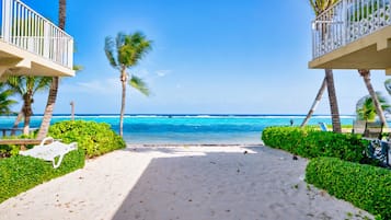 Vista sulla spiaggia con un sentiero che conduce verso l'oceano, palme e una sedia bianca.