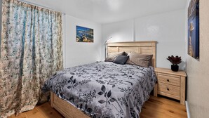 A bedroom with a bed, a nightstand, a lamp, a painting, and a curtain.