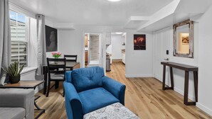 Ein modernes Wohnzimmer mit blauem Sofa, Esstisch und Stühlen, einer Treppe zum Küchenbereich und einem Flur mit einem gerahmten Bild an der Wand.
