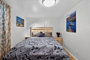 A bedroom with a bed, nightstand, and two wall-mounted pictures. - Midtown Reno Apartment | Near UNR & Downtown (Reno)