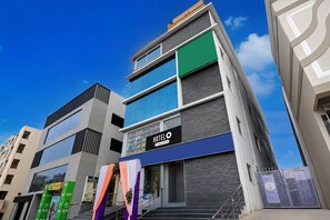 Un hotel de varios pisos con fachada moderna, amplias ventanas y una escalera visible que conduce a la entrada.