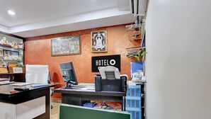 Een hotel receptie met een computer, een stoel en een balie. Er hangen afbeeldingen in lijsten aan de muur en een bord met de tekst 'HOTEL'.