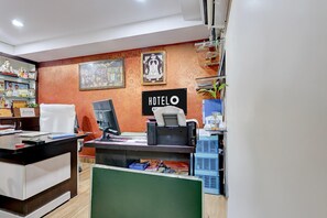 Un mostrador de recepción de hotel con una computadora, una silla y una barra. Hay cuadros en la pared y un cartel que dice 'HOTEL'.