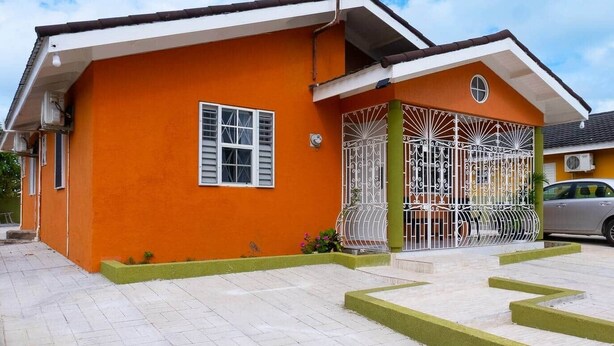 Uma casa com fachada laranja vibrante, entrada com portão e acesso por meio de um caminho de pedras.