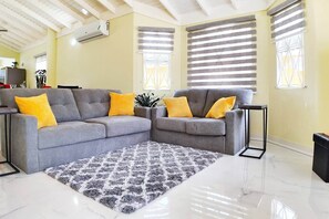 A living room with two grey sofas, yellow cushions, a patterned rug, and a black side table. - Elegant 2BR Retreat | Trelawny, Jamaica (Trelawny Parish)