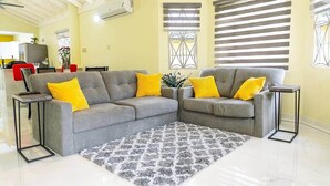 Uma sala de estar com dois sofás cinzas, almofadas amarelas, um tapete estampado e uma pequena mesinha.