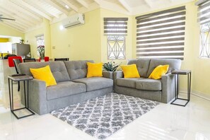 Ein Wohnzimmer mit zwei grauen Sofas, gelben Kissen, einem gemusterten Teppich und einem kleinen Beistelltisch.