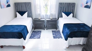 Quarto duplo com design moderno, duas mesas de cabeceira, janela com cortinas e obras de arte nas paredes.