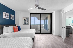 Quarto com cama, ventilador de teto, vista por uma porta de vidro e obras de arte nas paredes.