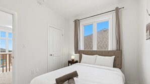 A bedroom with a bed, a window with curtains, a nightstand with a lamp, and a door leading to a balcony.