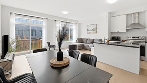 A modern kitchen with a dining area, large windows, and a view of a balcony.