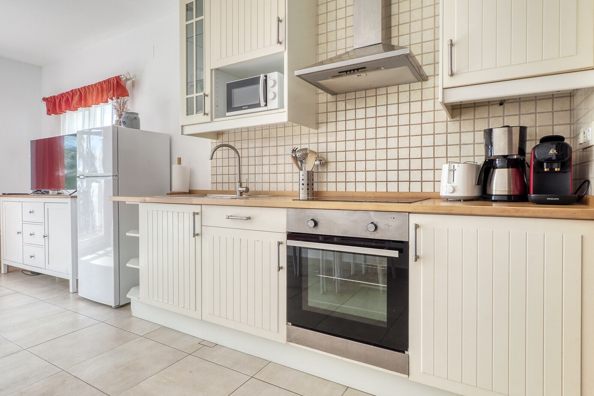 A modern kitchen with white cabinetry, a microwave, a stove, and a coffee maker.